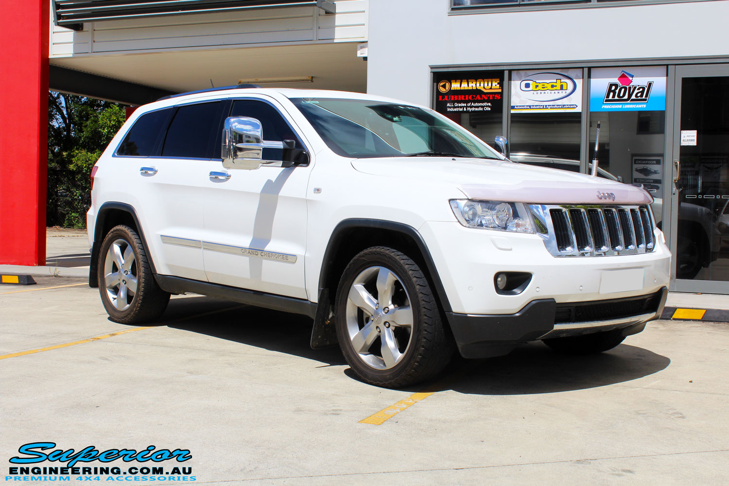 Right front side view of a White Jeep WK2 Grand Cherokee being fitted with an Airbag Man Coil Helper Air Kit Standard Height