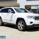 Right front side view of a White Jeep WK2 Grand Cherokee being fitted with an Airbag Man Coil Helper Air Kit Standard Height