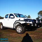 Right front side view of a White Isuzu D-Max Dual Cab being fitted with a Superior Remote Reservoir 2" Inch Lift Kit, Airbag Man Leaf Air Kit, Ironman 4x4 Bullbar + Side Steps, VRS Winch, Safari Snorkel + King Wheels & Nitto Tyres