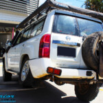 Rear left side view of a White Nissan GU Patrol Wagon flexed up before fitment of a Superior Nitro Gas 2" Inch Lift Kit, Coil Tower Brace Kit, Superior Hybrid Superflex Radius Arms, Airbag Man Coil Air Kit and Superior Adjustable Hollow Bar Drag Link