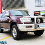 Right front side view of a Maroon Toyota 105 Series Landcruiser Dual Cab before fitment of a Superior Nitro Gas 3" Inch Lift Kit with Airbag Man 3" Coil Air Kit