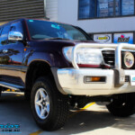 Right front side view of a Maroon Toyota 105 Series Landcruiser Dual Cab after fitment of a Superior Nitro Gas 3" Inch Lift Kit with Airbag Man 3" Coil Air Kit