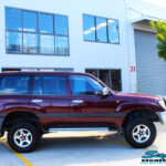 Right side view of a Maroon Toyota 105 Series Landcruiser Dual Cab after fitment of a Superior Nitro Gas 3" Inch Lift Kit with Airbag Man 3" Coil Air Kit