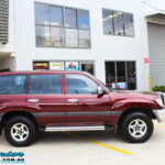 Left side view of a Maroon Toyota 105 Series Landcruiser Dual Cab before fitment of a Superior Nitro Gas 3" Inch Lift Kit with Airbag Man 3" Coil Air Kit